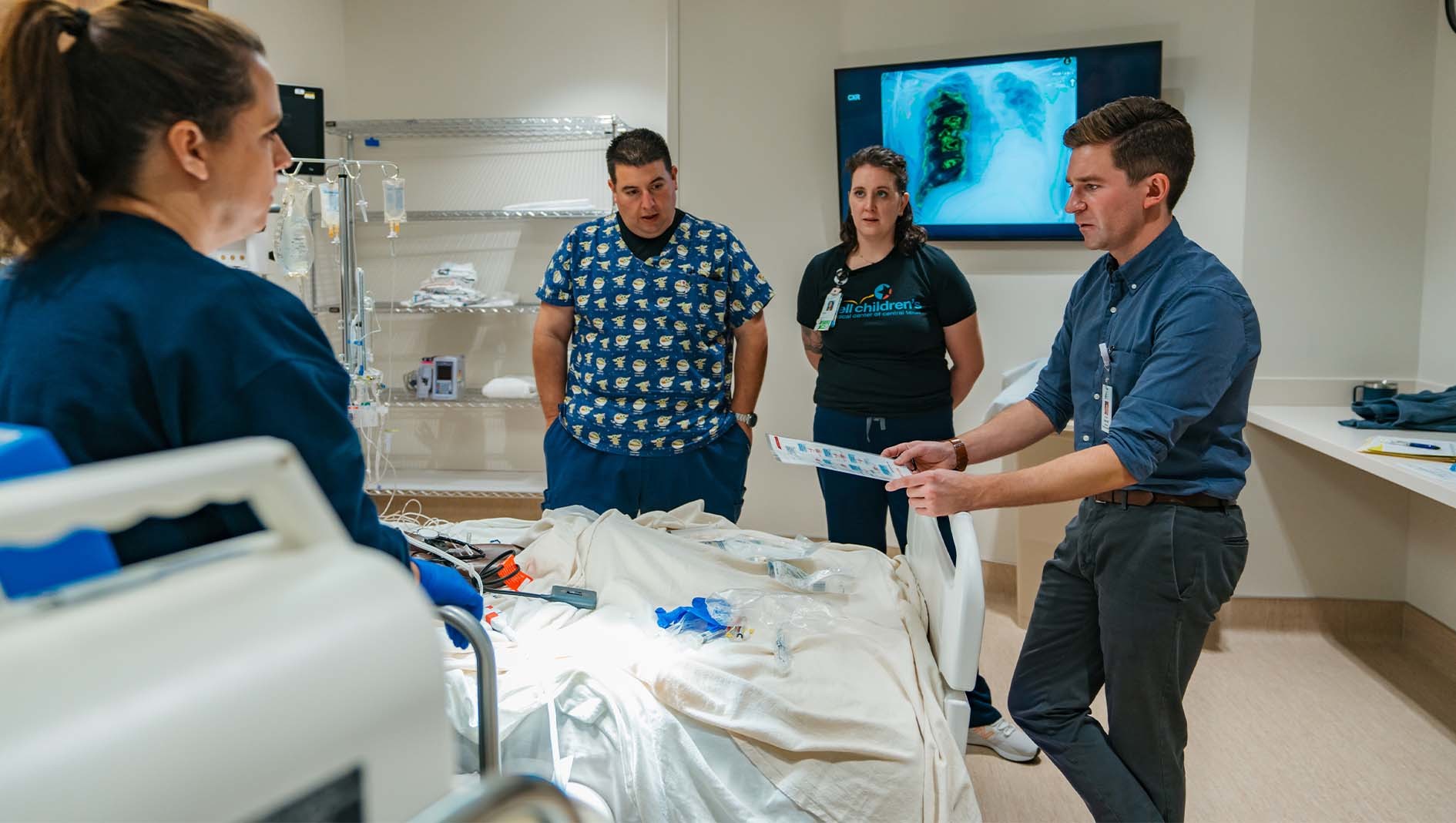 Medical professionals stand and have a discussion around a medical bed within the Dell Children's Simulation Center.