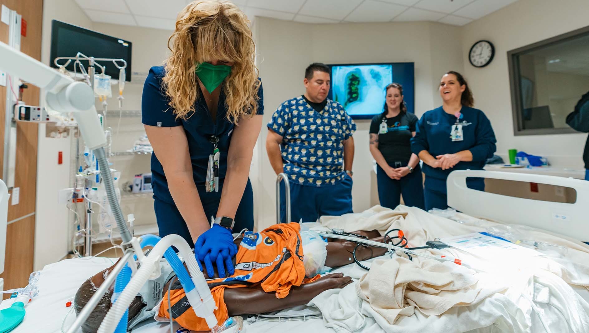 A woman performs CPR on a manikin in the Dell Children's Simulation Center while other medical professionals look on.