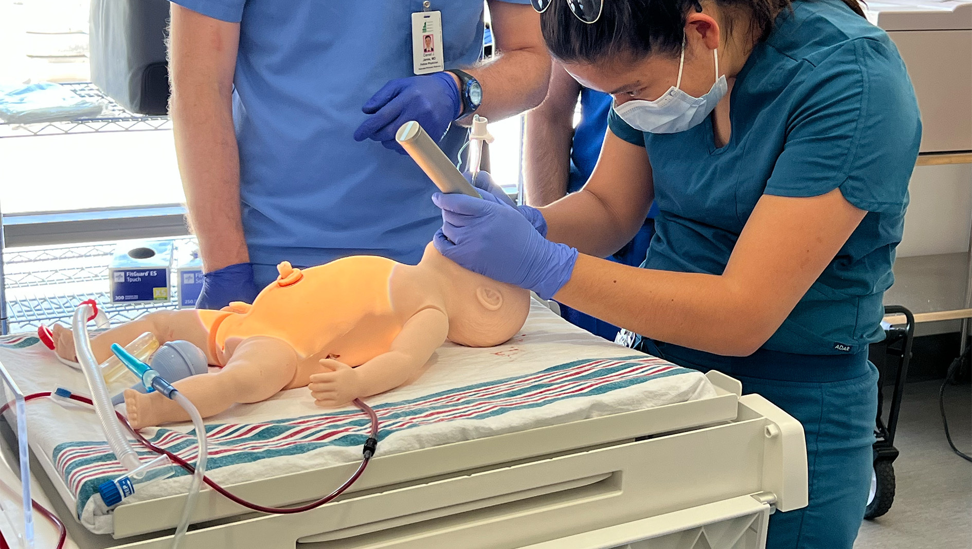 A woman medical trainee wearing green scrubs performs a medical procedure on a mannequin.