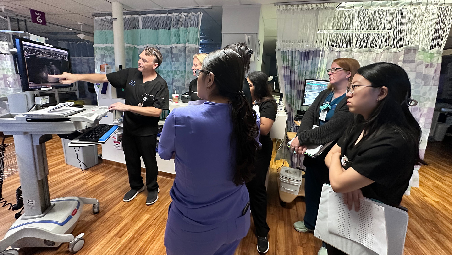 NICU fellows listen to faculty member as he instructs POCUS procedure.