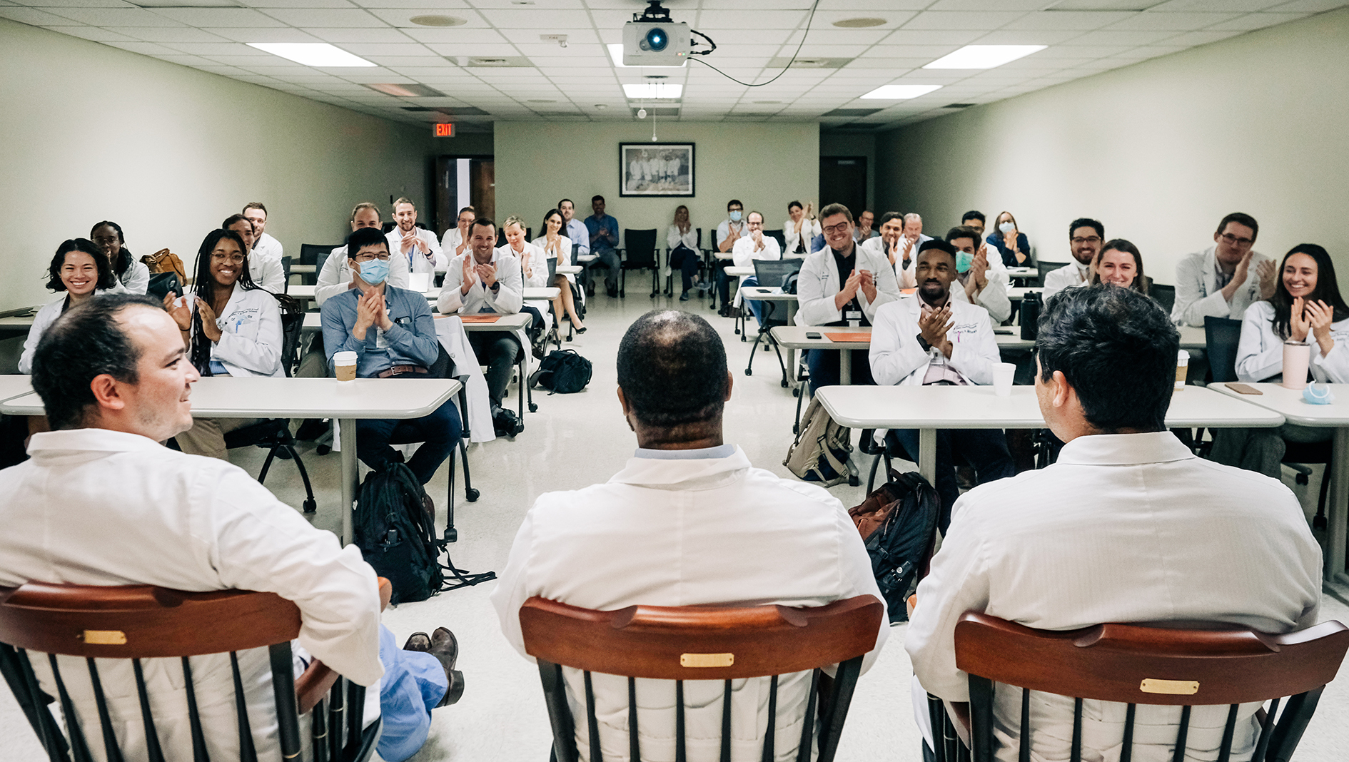 Surgery residents listen to a lecture by three physicians