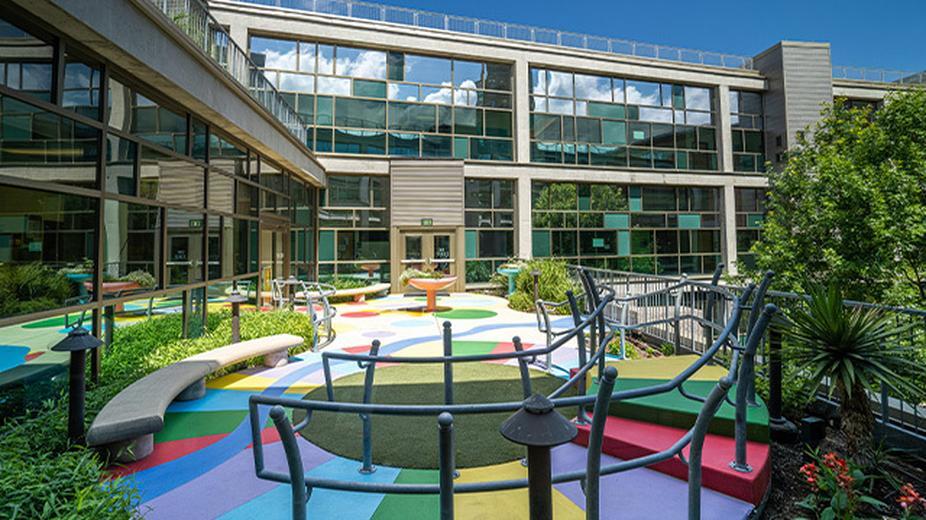 An exterior view of a side of Dell Children's Medical Center with lots of windows. In the foreground, an outdoor playground area.