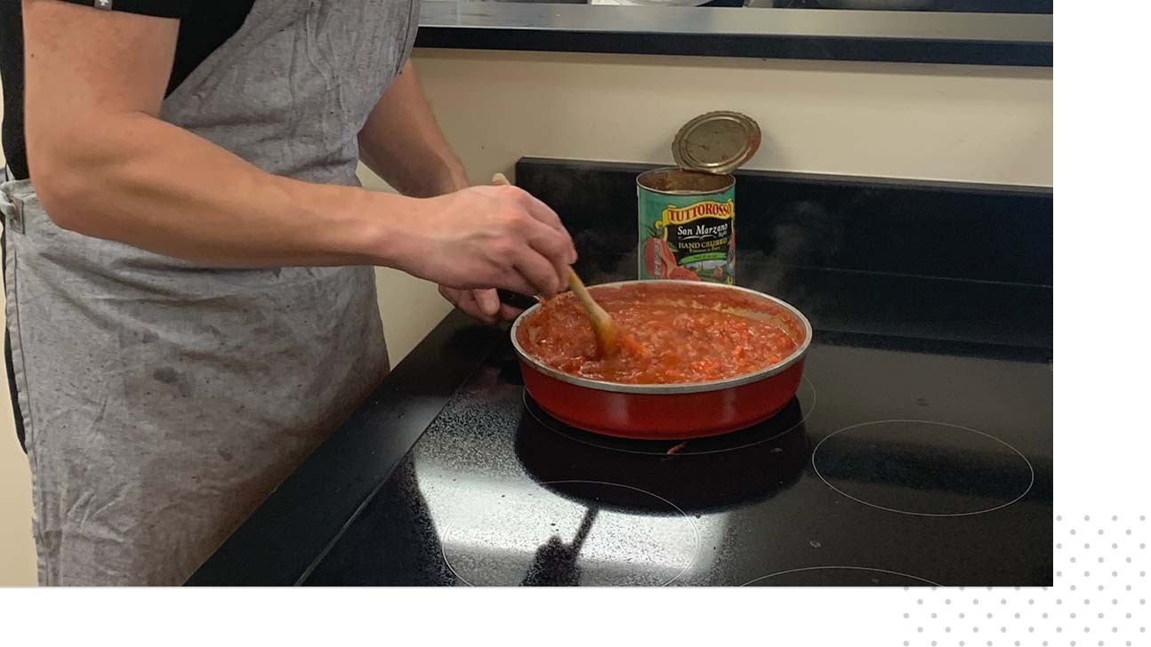 A man stirs a tomato-based dish atop an induction stovetop.