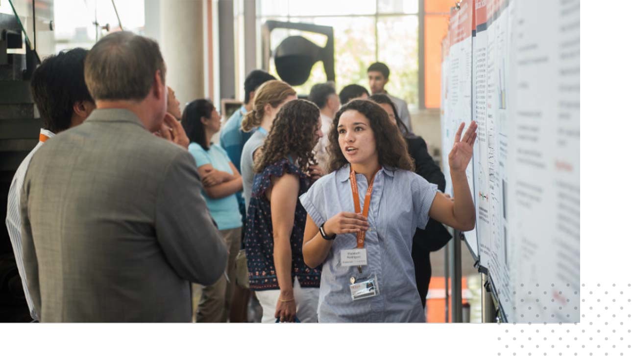 A student presents a research poster to an event attendee.