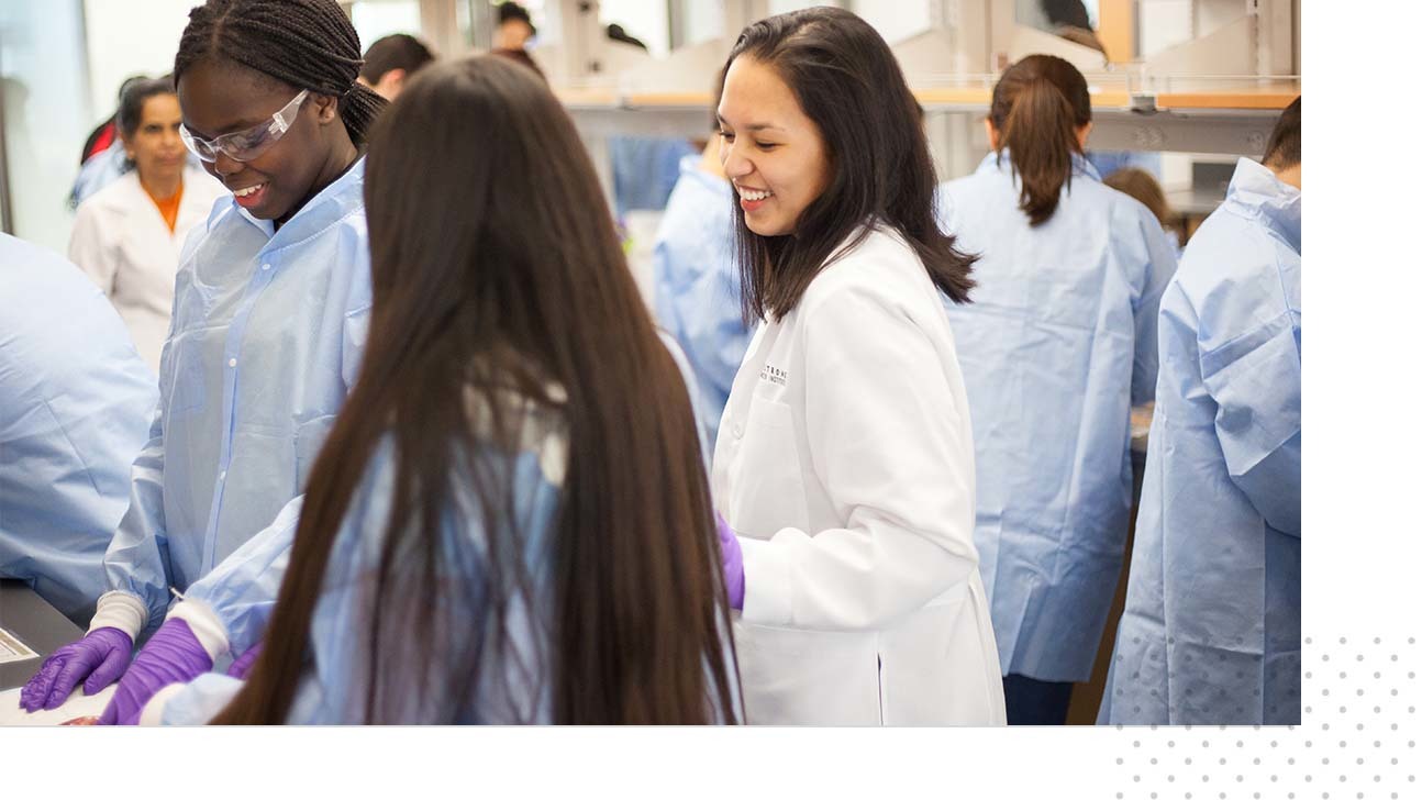 Several young students wear laboratory overcoats and participate in chemistry activities during an Explore UT event.
