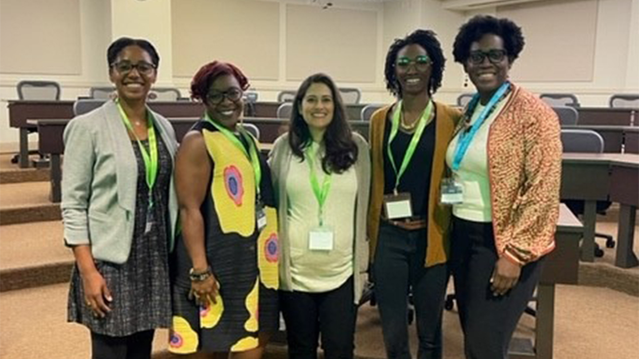 Five women stand together for a photo in a lecture hall.