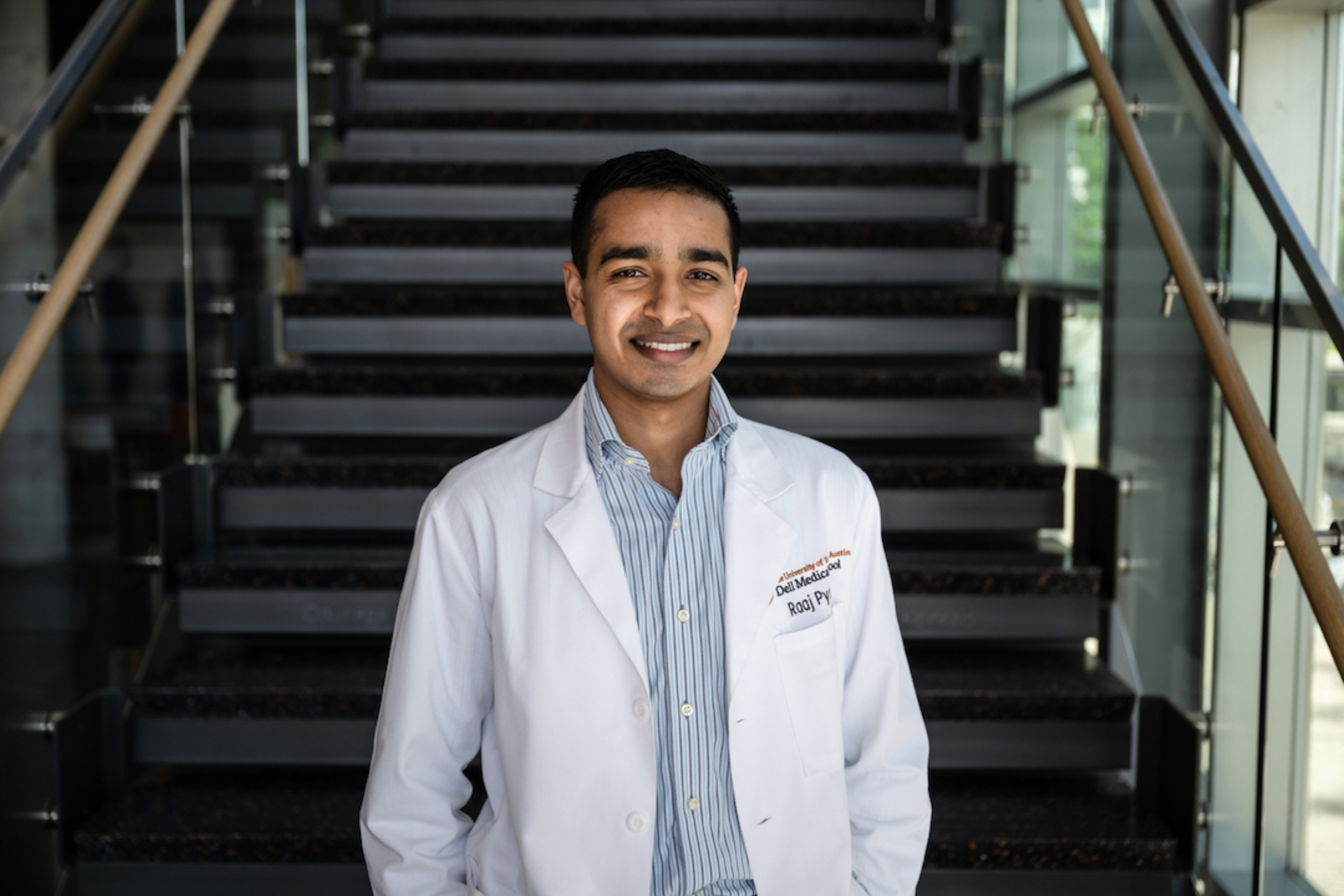 Raaj Pyada smiles at the camera in a medical student's white coat.