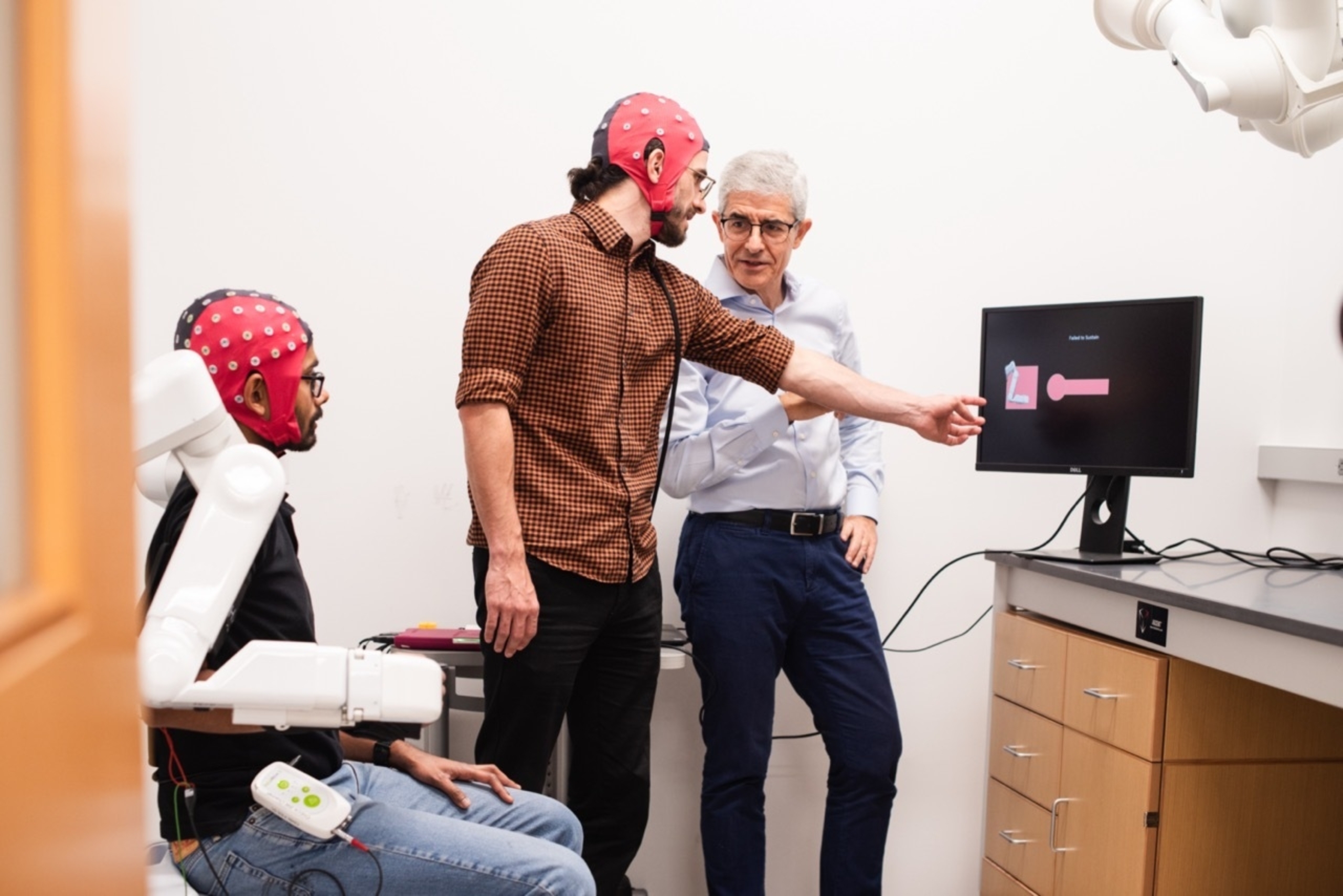 Researcher José del R. Millán and two graduate students wearing electrode caps, huddle around a computer monitor.