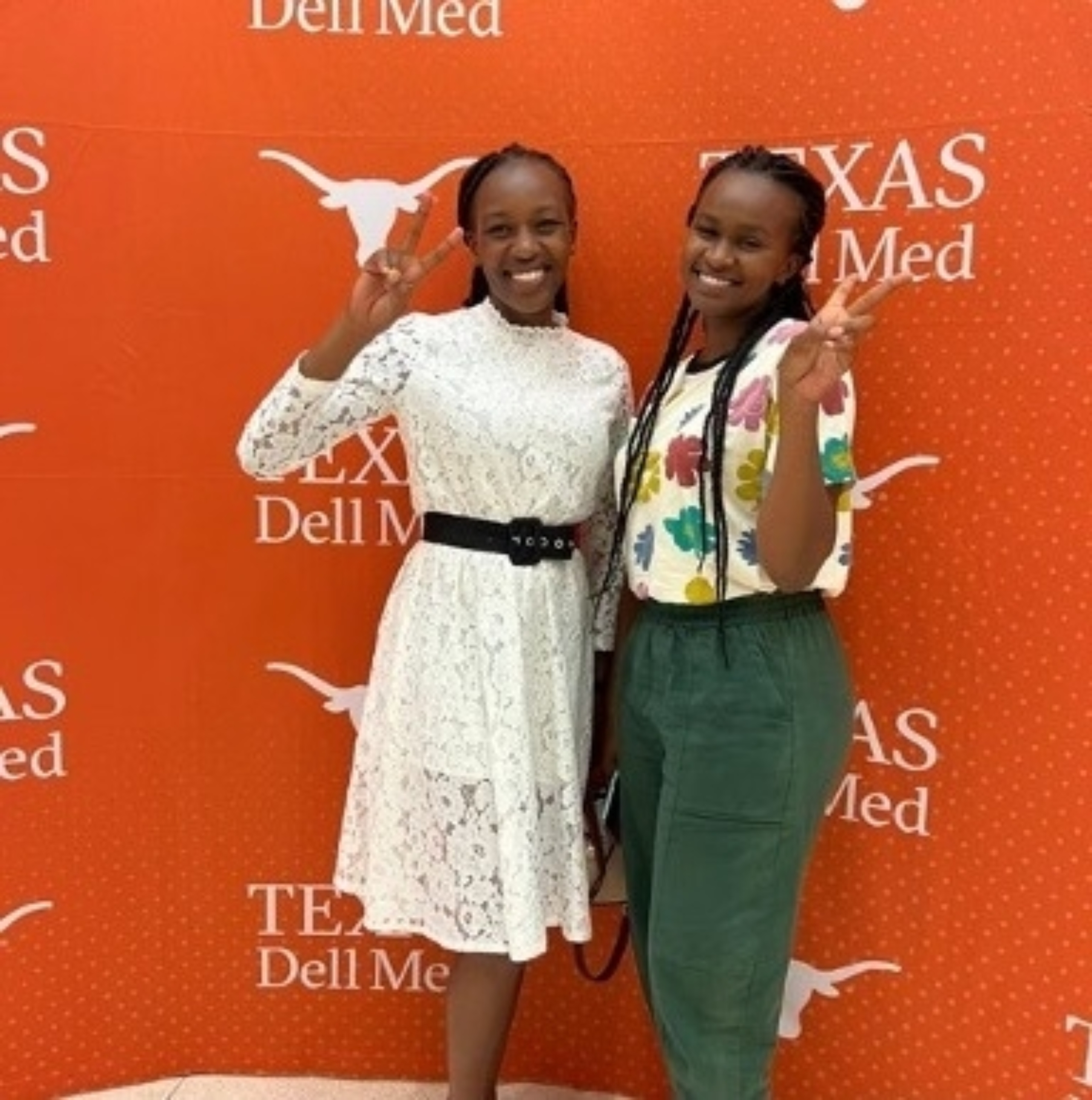 Two international exchange students from Kenya stand together for a photo in front of a burnt orange Texas Dell Med backdrop.
