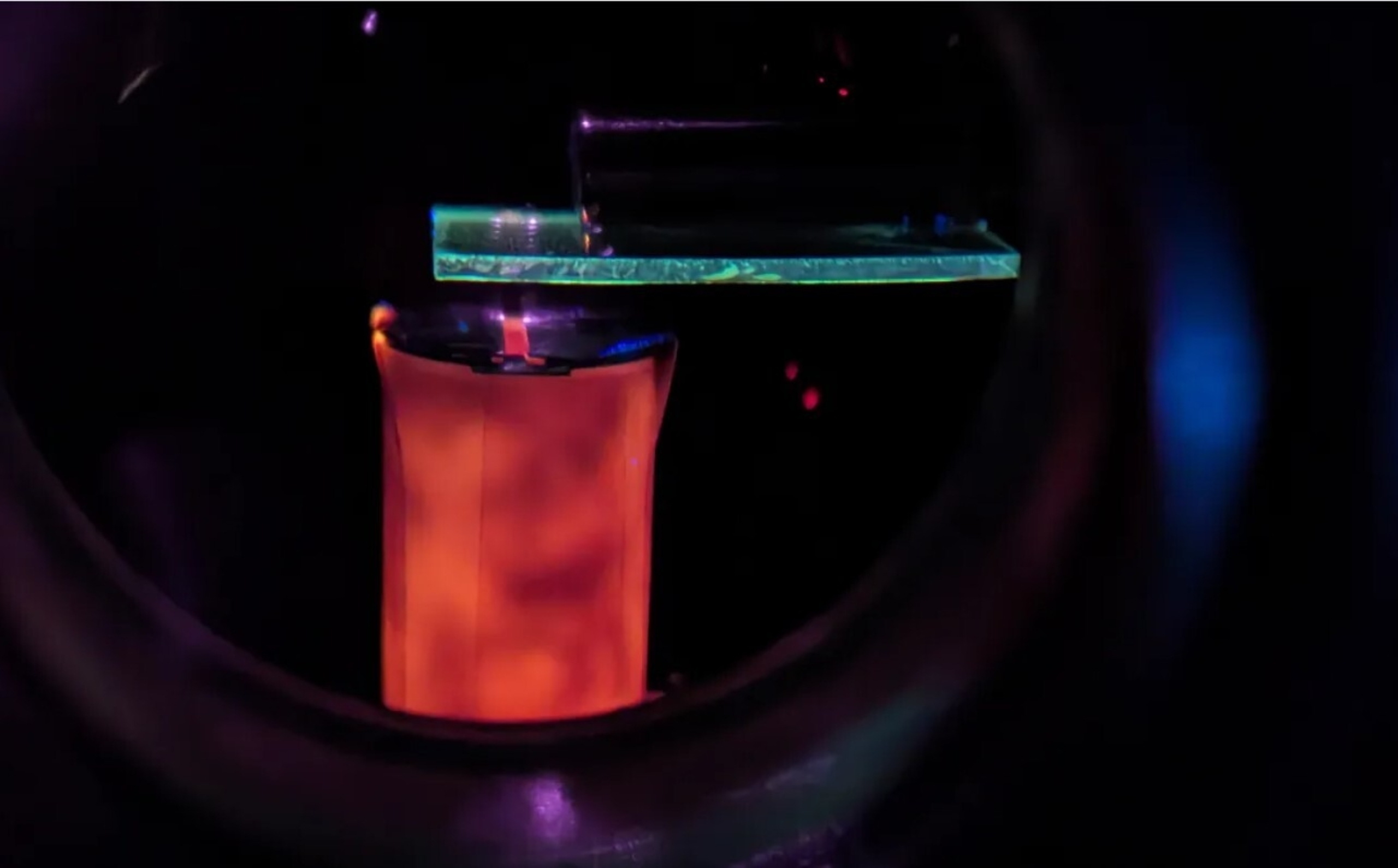 Image shows a laser tool, with a column of reddish material representing laser ablation of a powdered sample. 