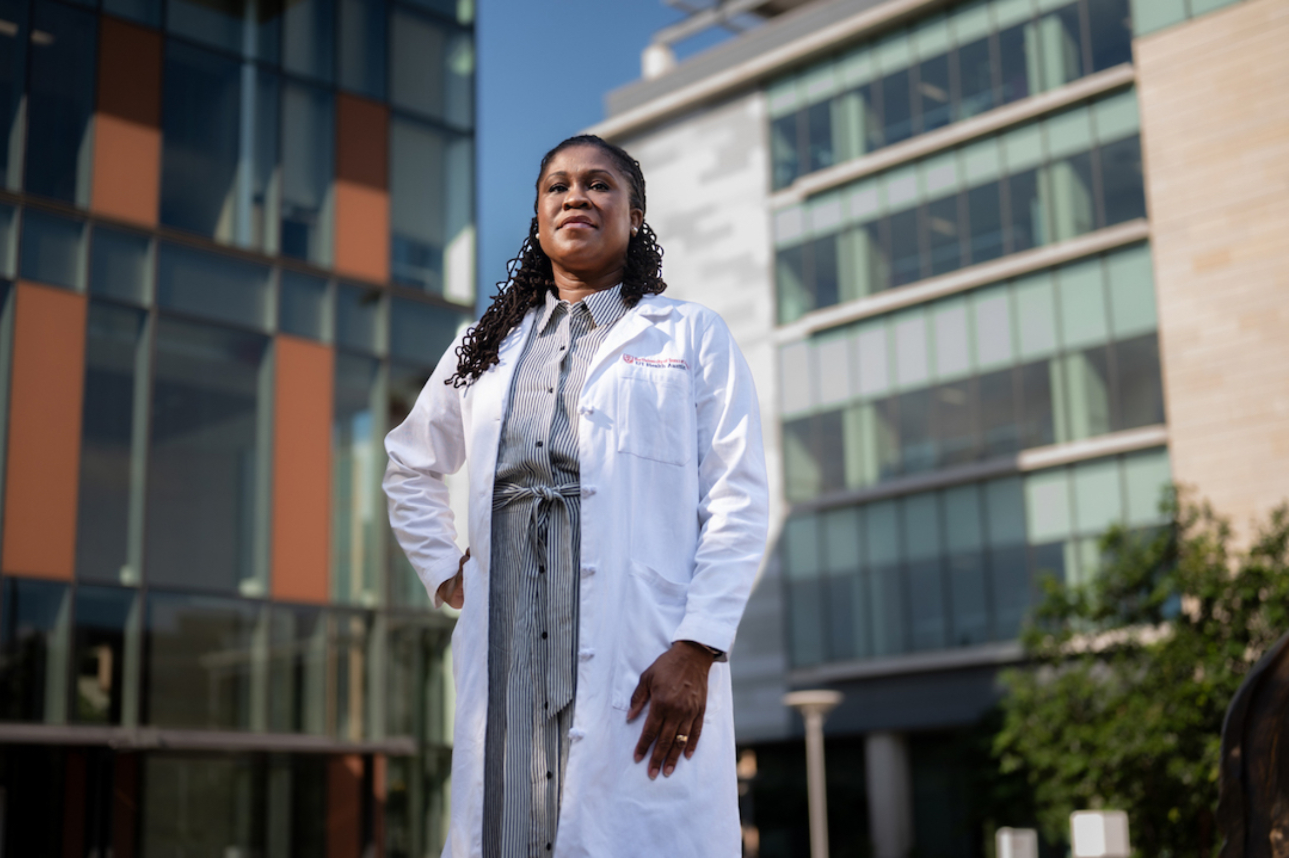 Akua Afriyie-Gray, M.D., stands in the Dell Med courtyard in a white physician's coat.
