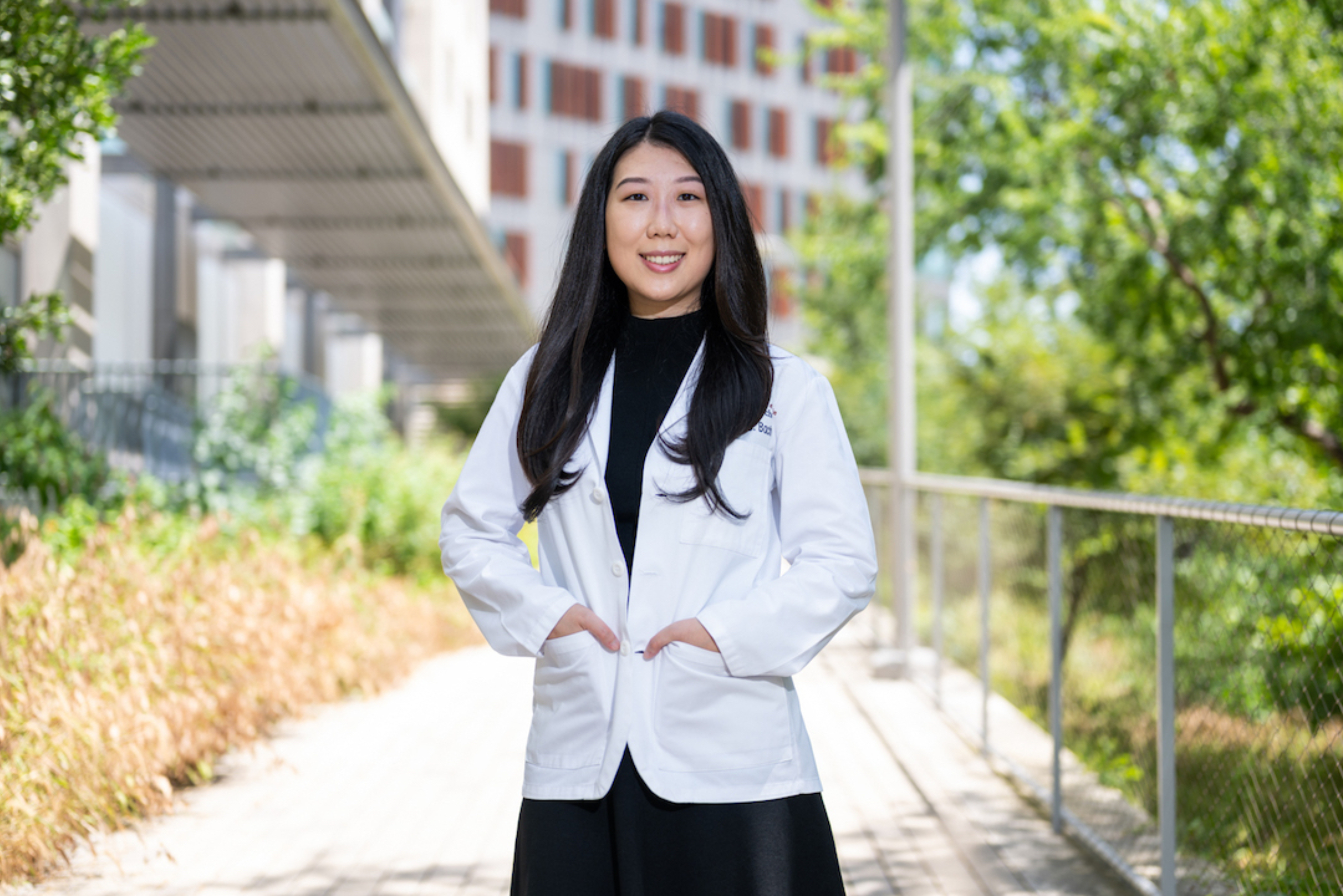 Image: Michelle Bach stands in a white coat on the Dell Medical School campus.