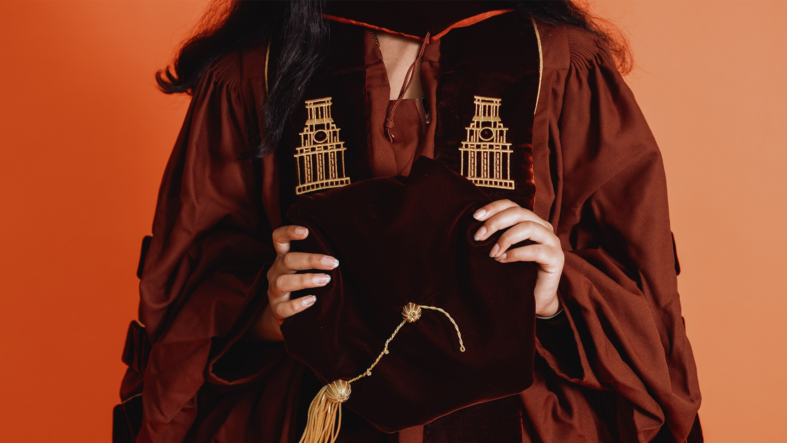 A close-up of a Dell Med student's hands holding a graduation cap while wearing regalia.