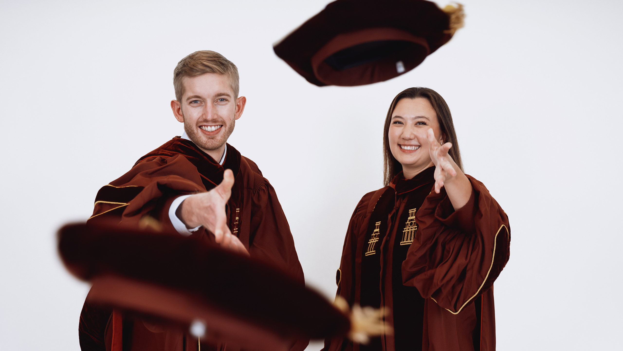 Two Dell Med students wearing graduation regalia and posing in celebratory fashion.