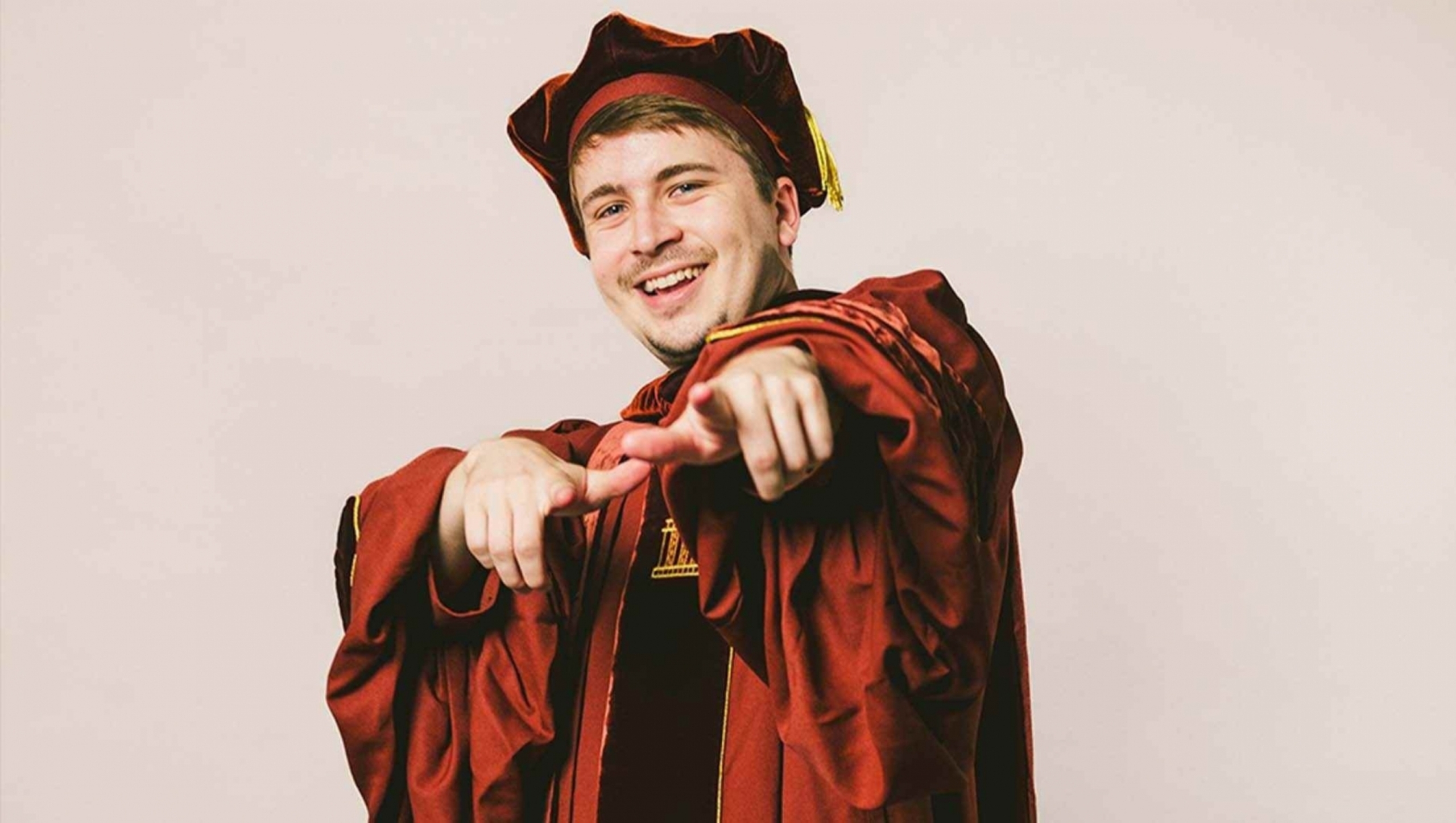 Ben Wroblewski in a celebratory pose while wearing graduation regalia.