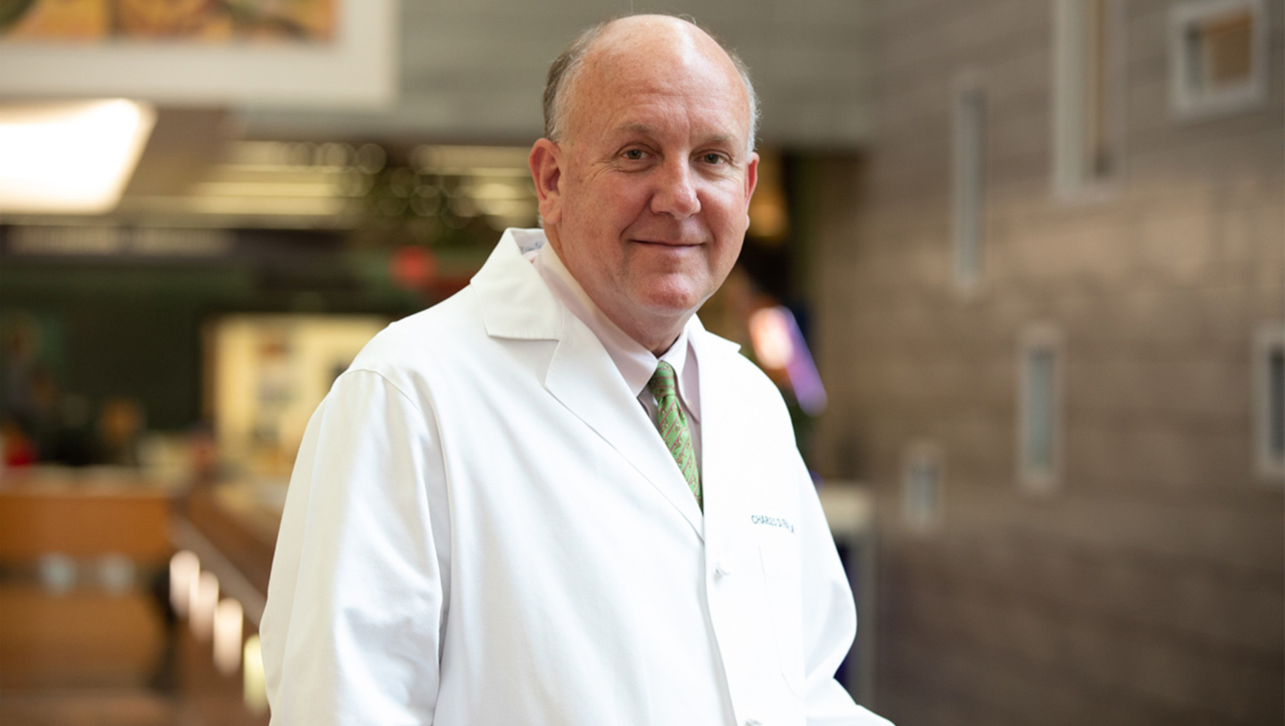 Charles Fraser, wearing a white medical coat, stands for a portrait inside a hospital.