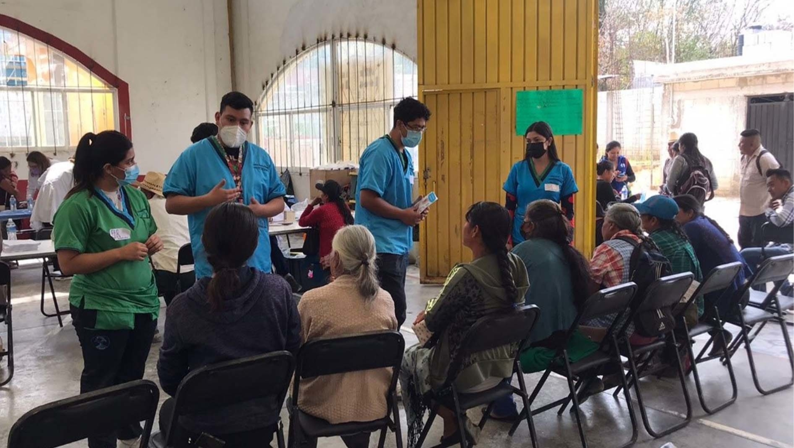 A number of medical professionals in scrubs having discussions with people seated in foldable chairs.