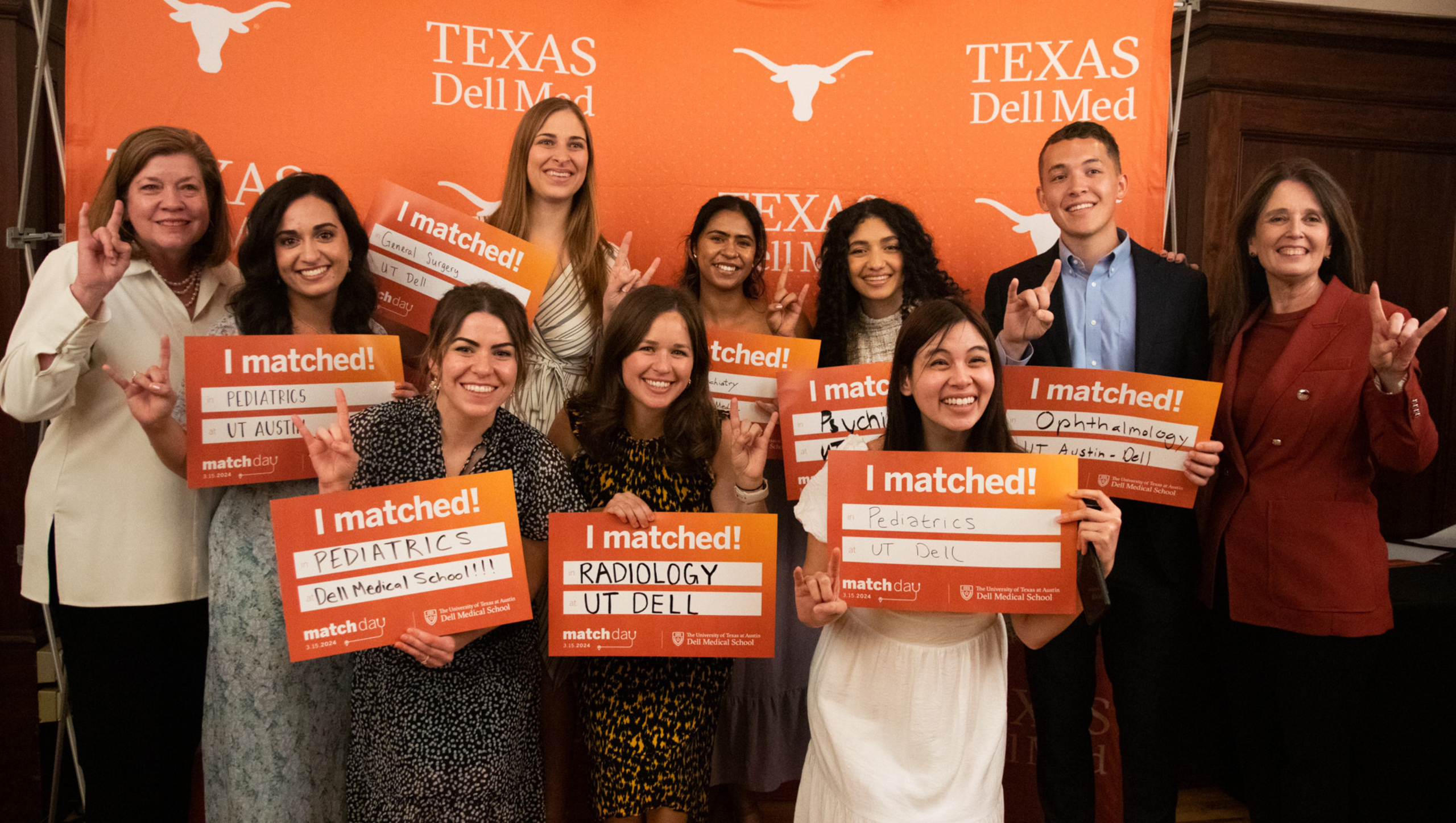 Dell Med students stand together for a group portrait holding up signs indicating which residency programs they matched to.