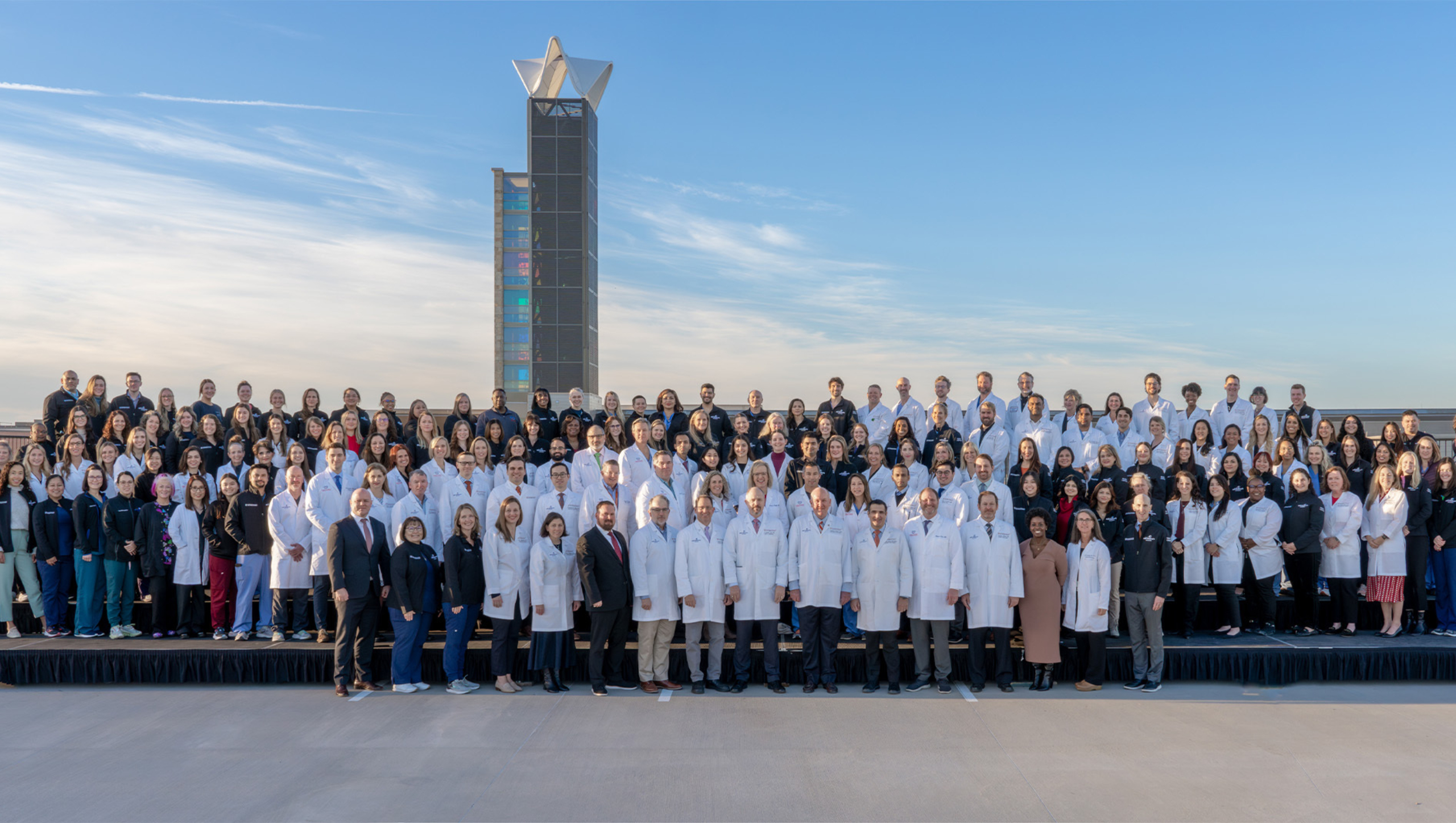 Faculty and medical professionals affiliated with the Pediatric Cardiac Critical Care Fellowship stand in rows for a team portrait outside and on the top of a building.