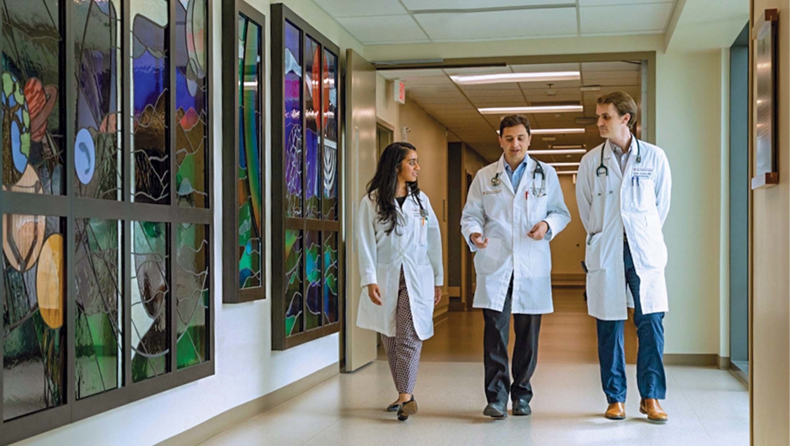 Two residents walk down a hall with a Dell Medical School faculty member for morning rounds.