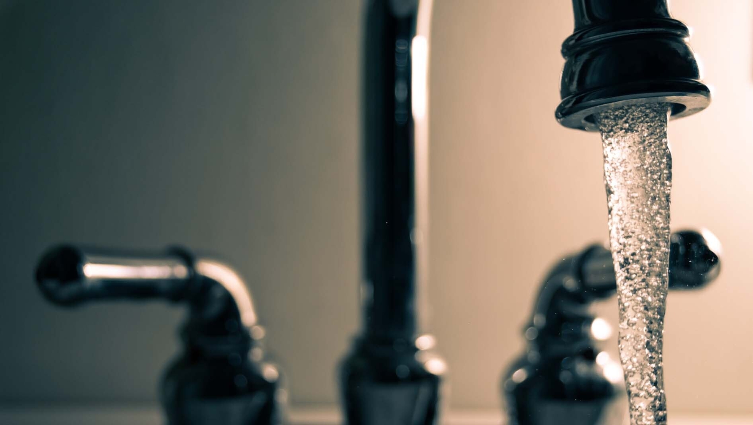 Water faucet in the on position with water streaming out,