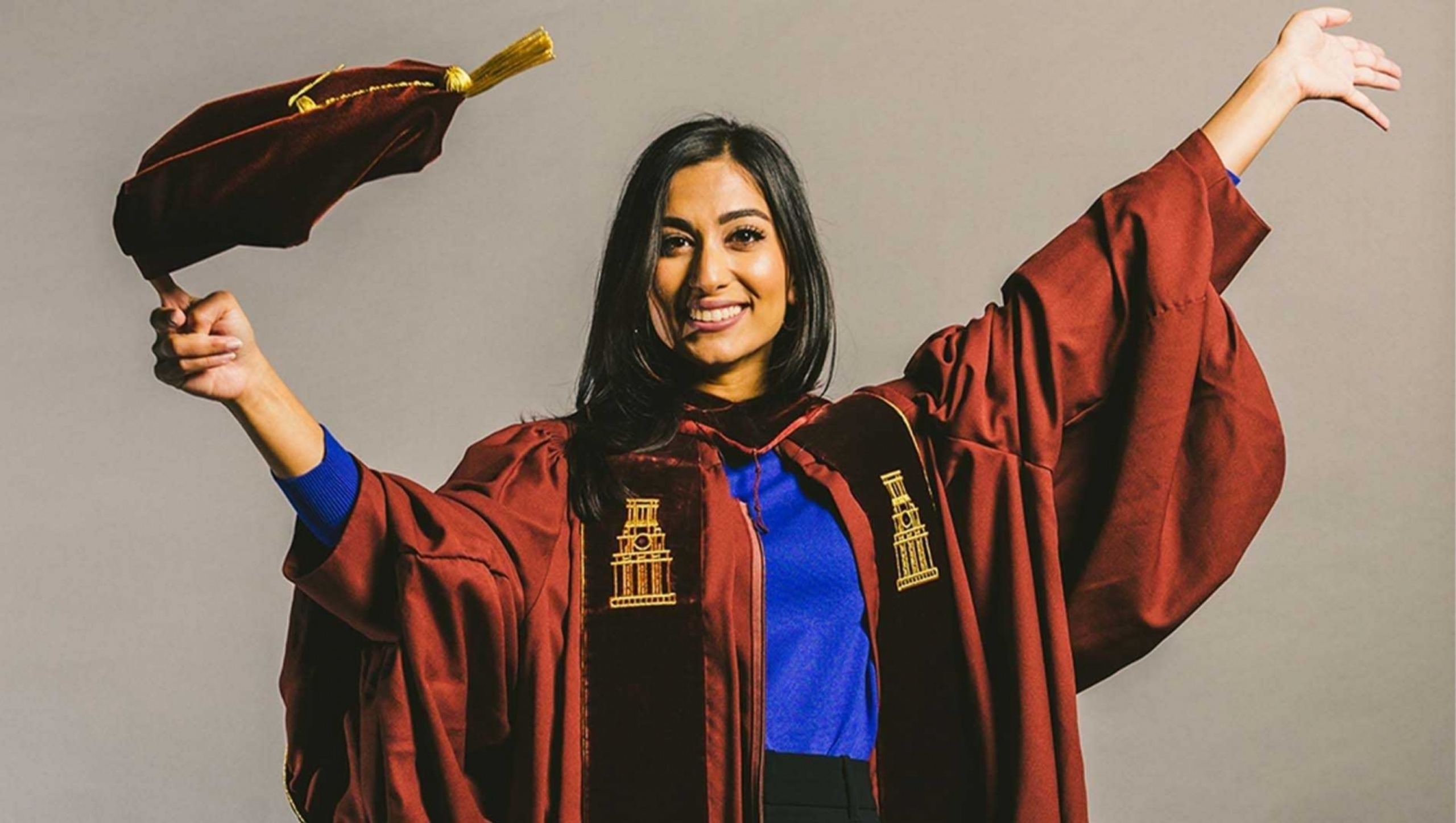 Zarra Qasim in a celebratory pose while wearing graduation regalia.