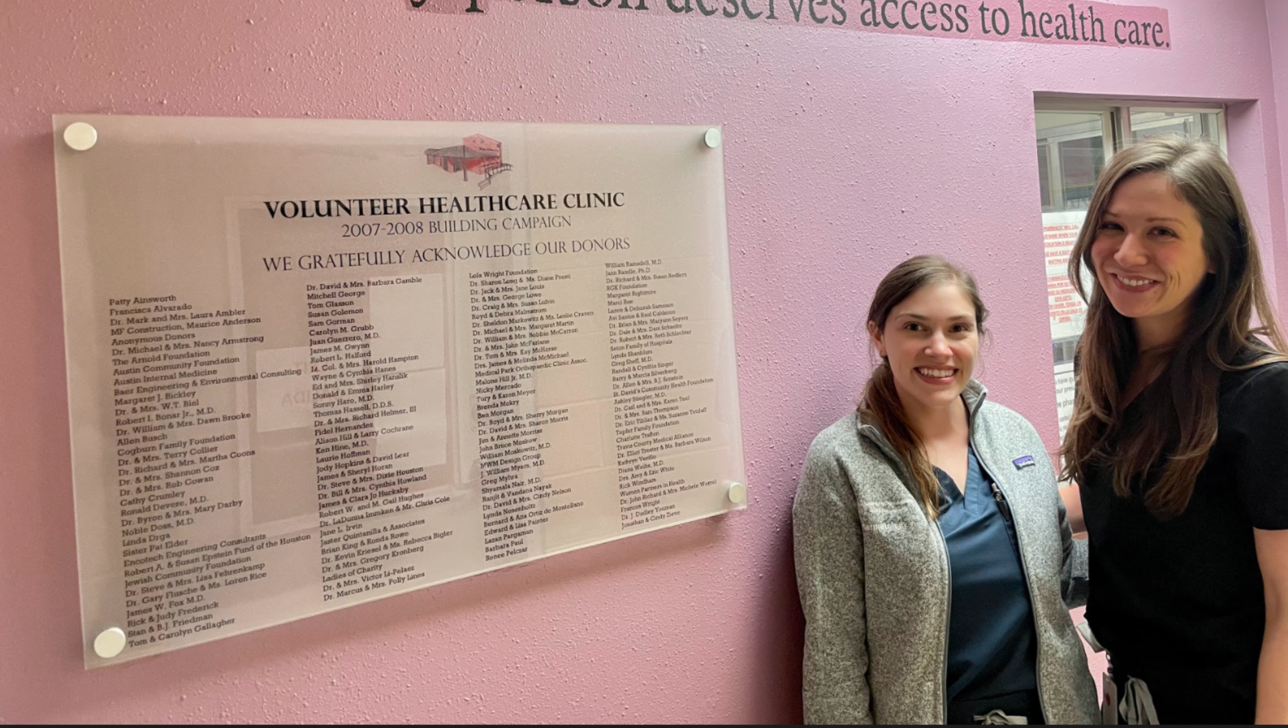Two dermatology residents pose in front of a wall highlighting community volunteers. 