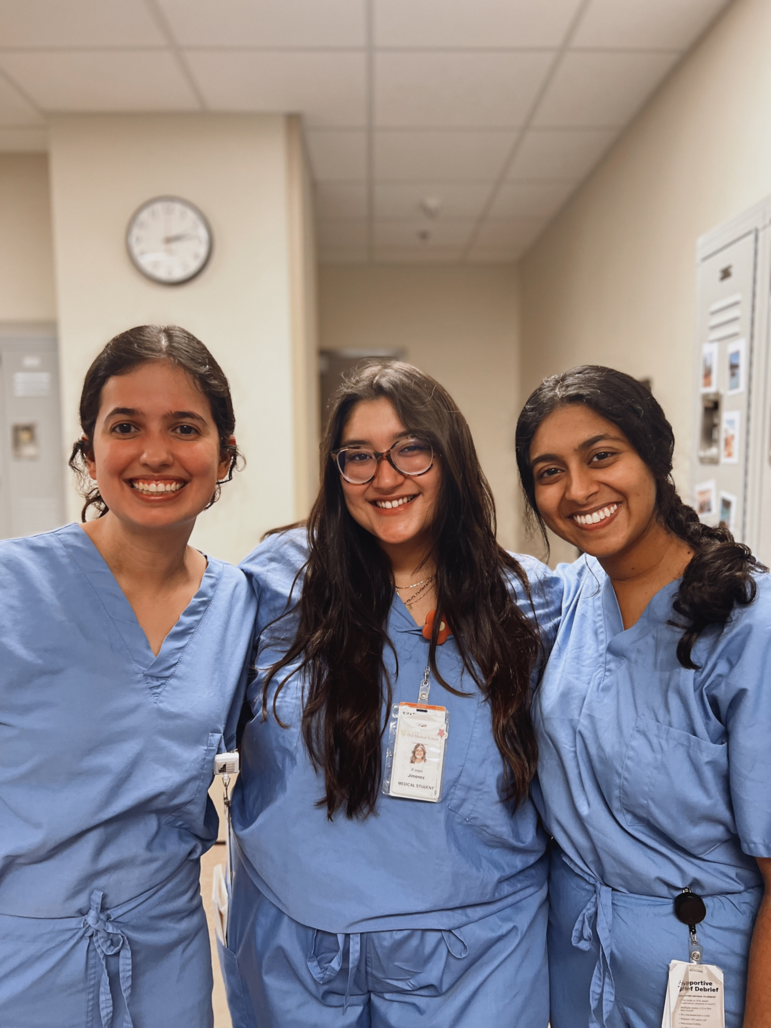 Three Dell Medical School students, all women and wearing blue scrubs, gather for a group photo.