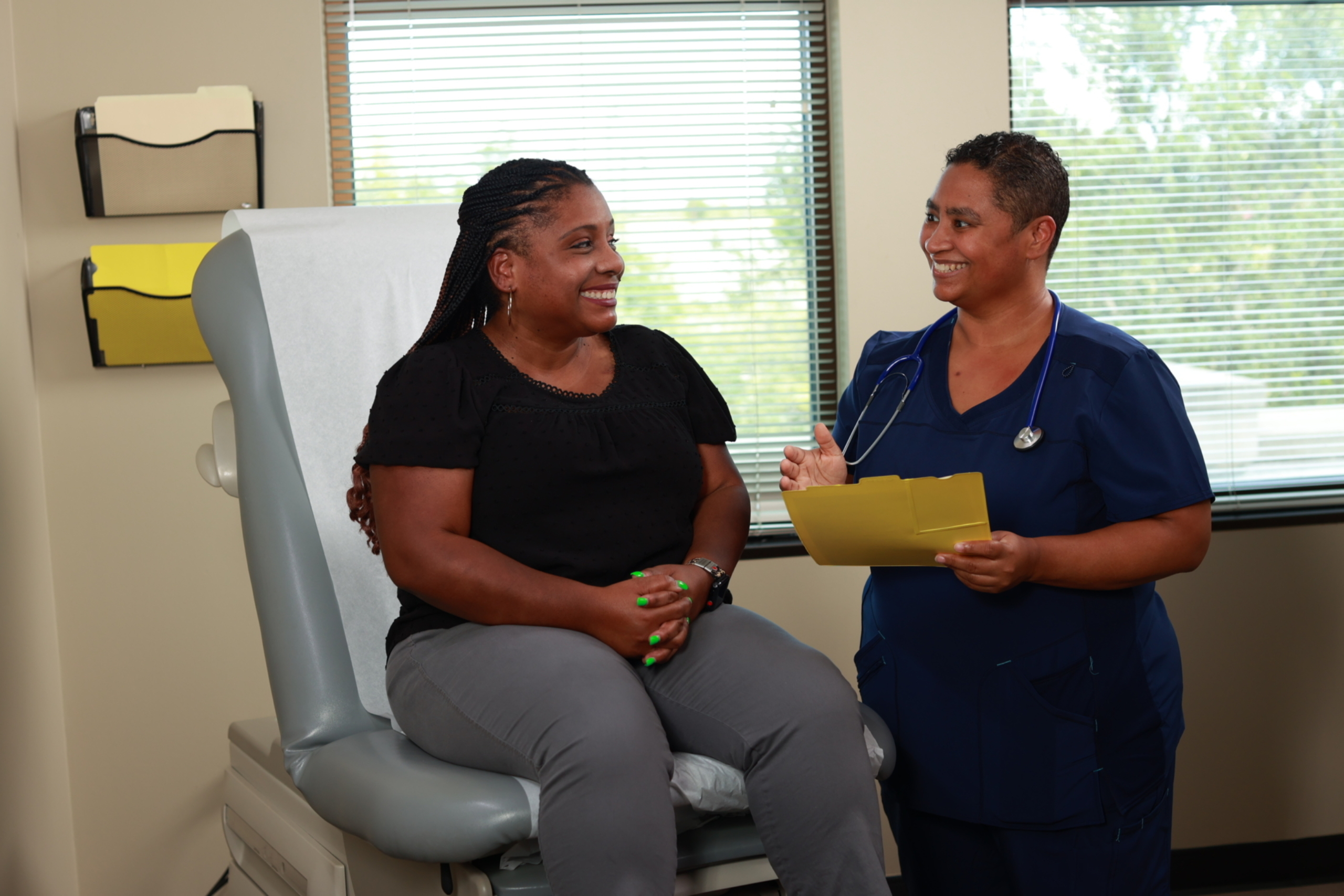 Female patient seated in exam room with female clinical provider standing next to her