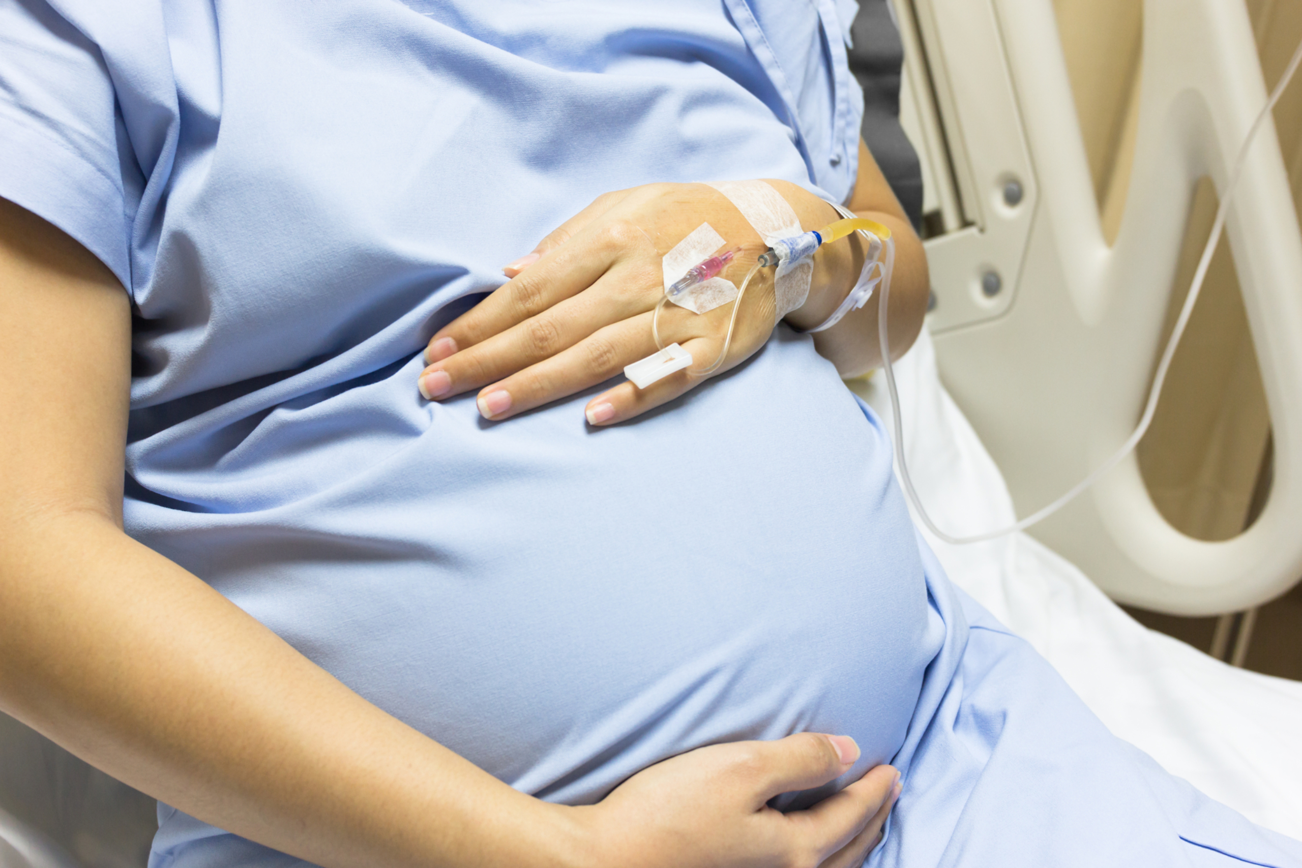 Pregnant woman receives an IV drip while sitting in hospital bed. 