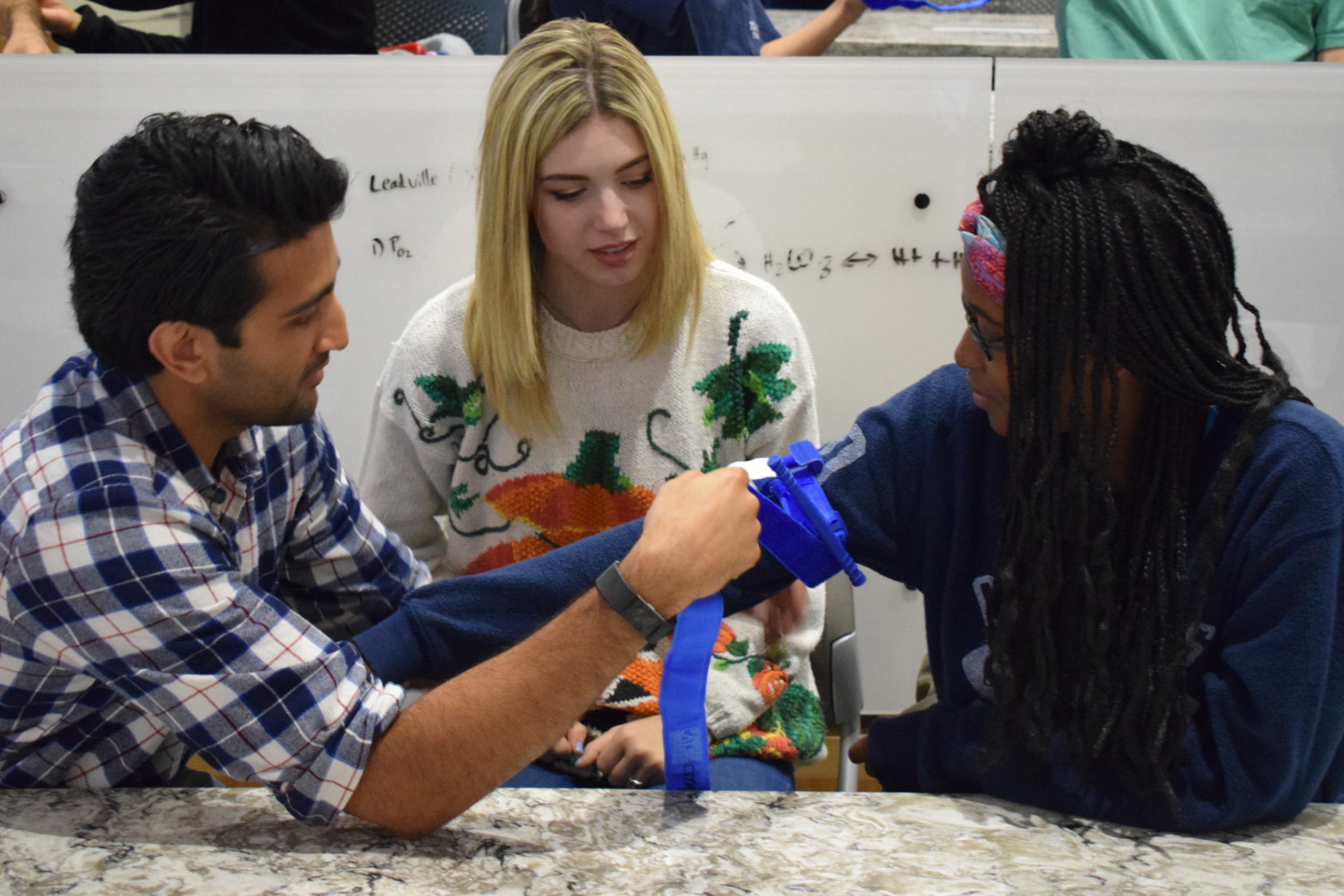 Three students learning to apply a tourniquet.