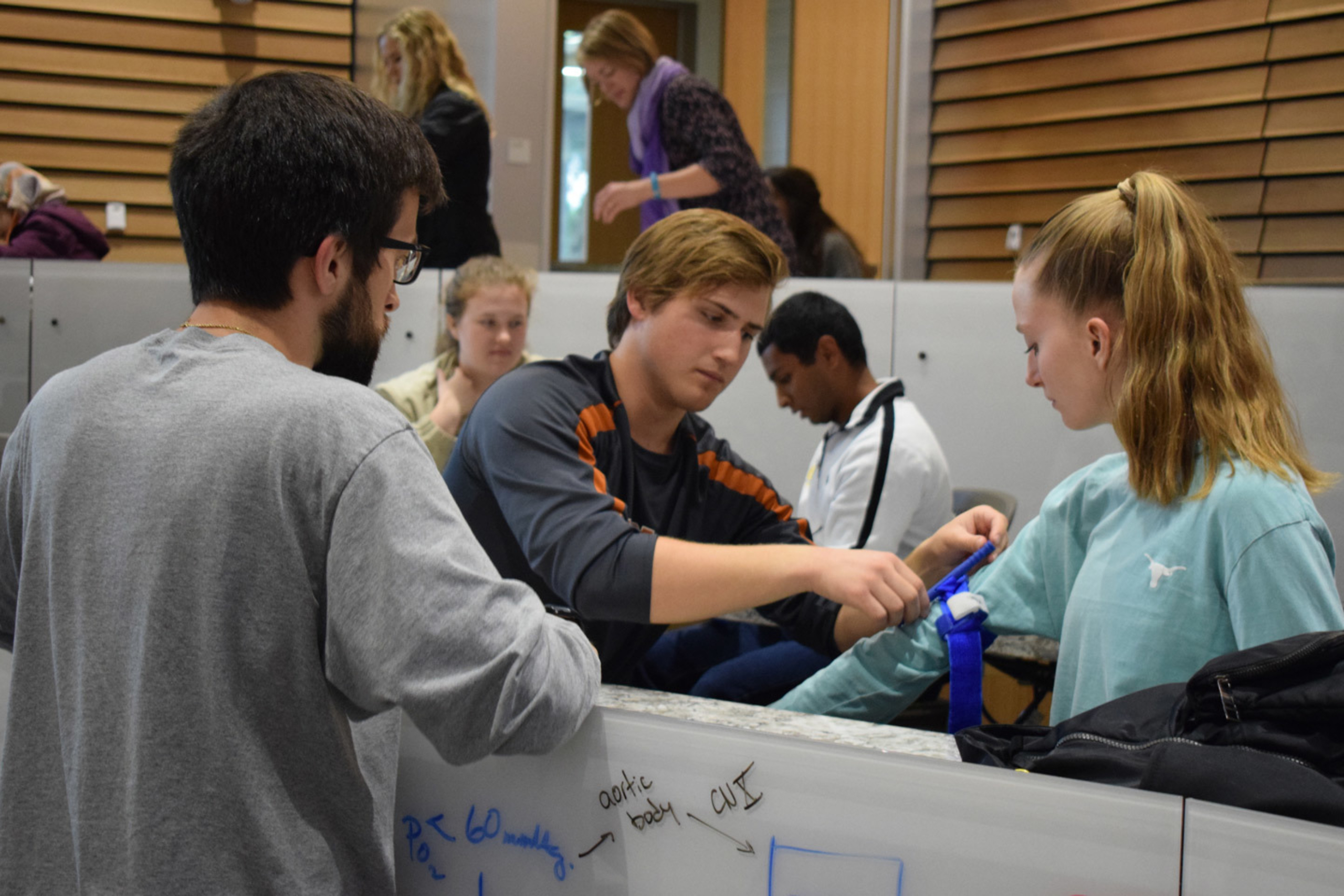 Three students learning to apply a tourniquet.