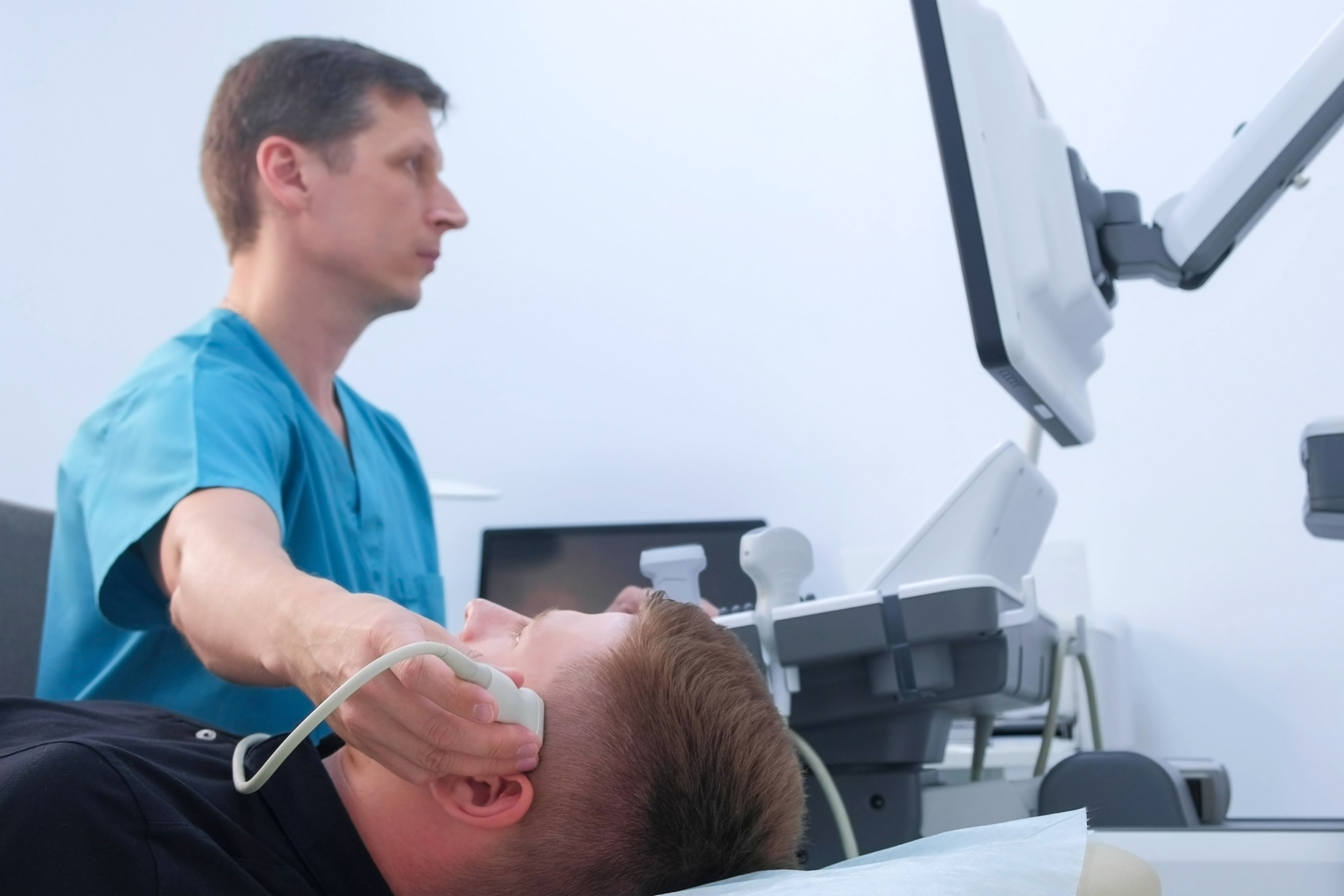 Doctor performs ultrasound on head of male patient.