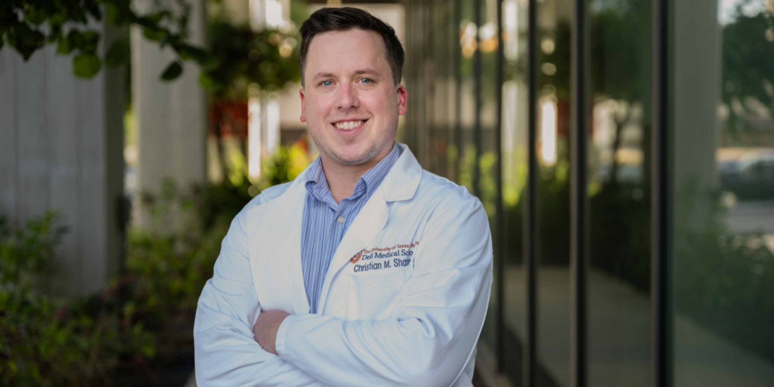 Christian Shannon, wearing a medical student white coat, stands for a portrait on the Dell Med campus.